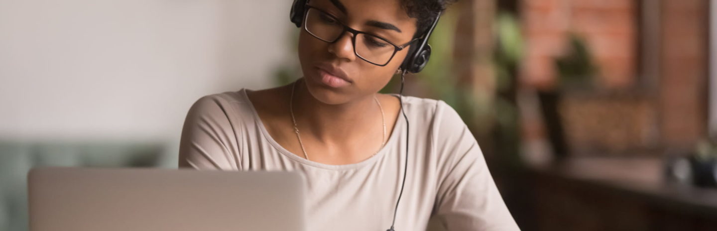 A younger girl studying at a desk with headphones and a laptop