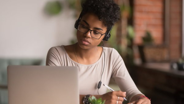 A younger girl studying at a desk with headphones and a laptop